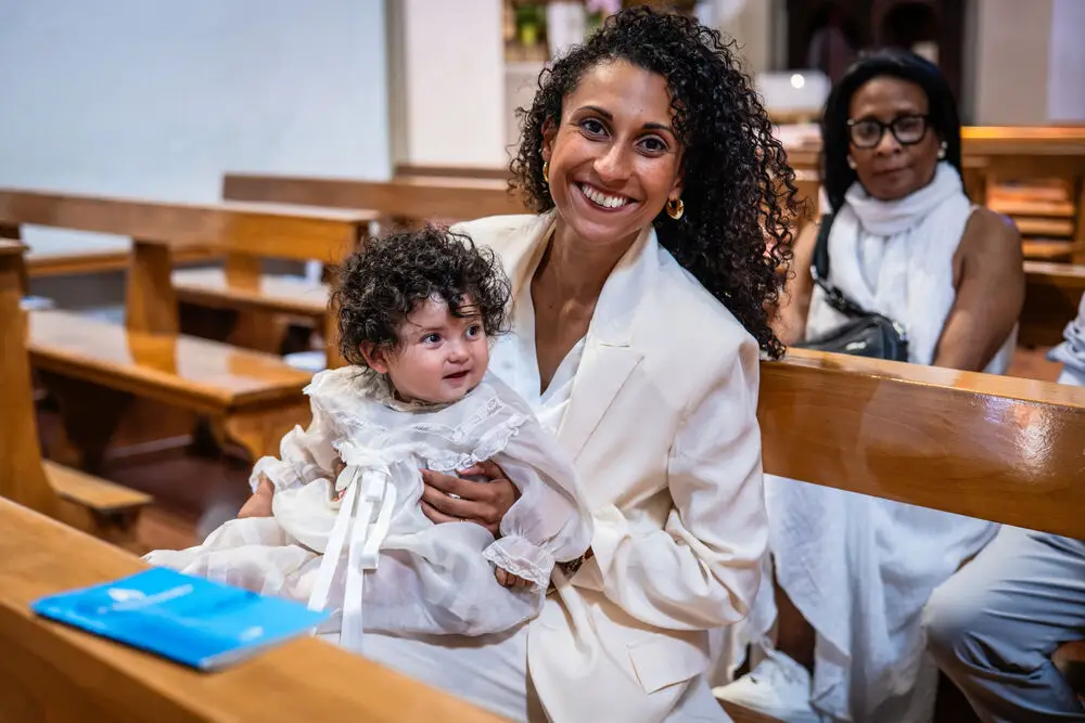 foto battesimo con mamma sorridente e neonata in abito bianco in chiesa