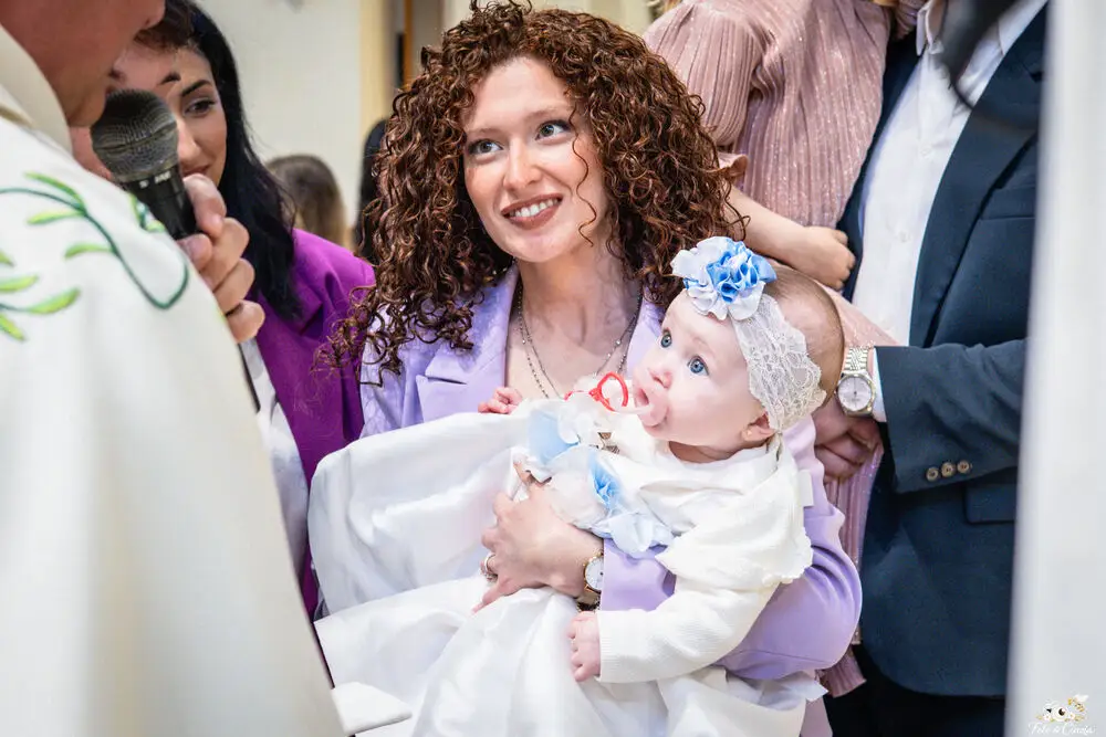 foto battesimo con mamma e neonata con fascia fiorata durante la cerimonia