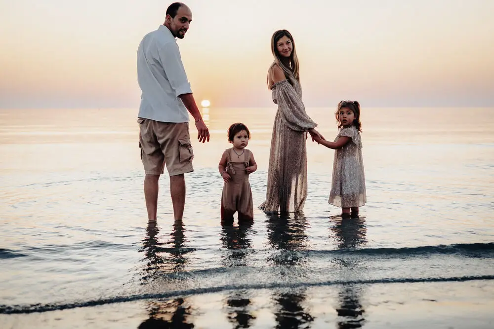 foto famiglia con genitori e due bambini mano nella mano nell'acqua del mare al tramonto