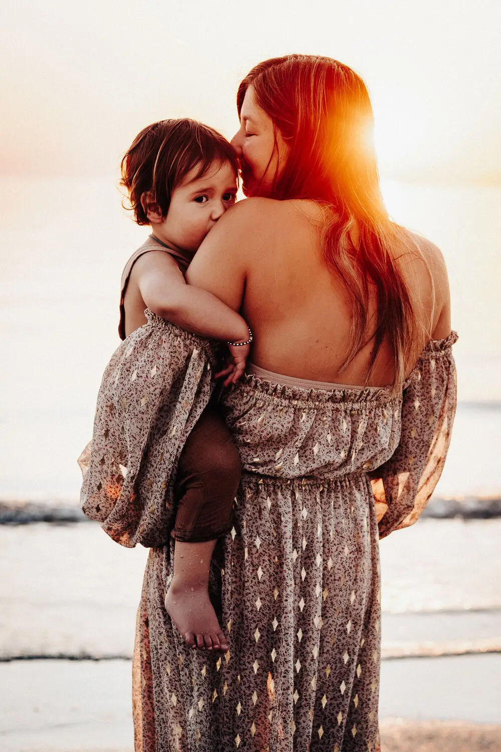 foto famiglia con mamma che abbraccia il bambino in spiaggia al tramonto
