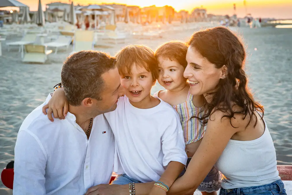 foto famiglia con genitori e due bambini abbracciati e sorridenti in spiaggia