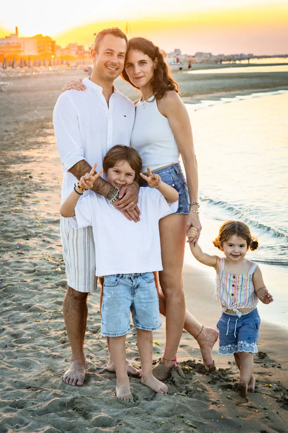 foto famiglia con genitori e bambini che camminano sulla spiaggia al tramonto