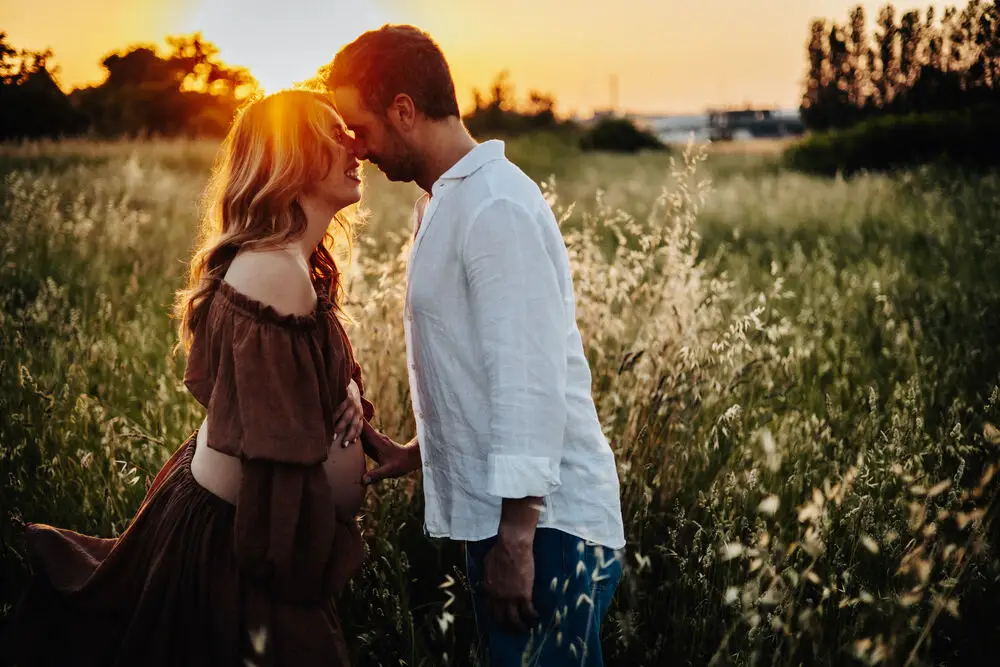 foto maternity con coppia fronte a fronte in un campo al tramonto