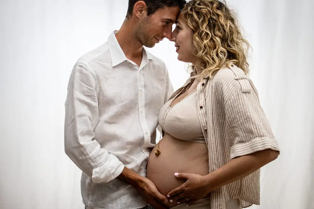 foto maternity con coppia abbracciata e mano sul pancione in studio
