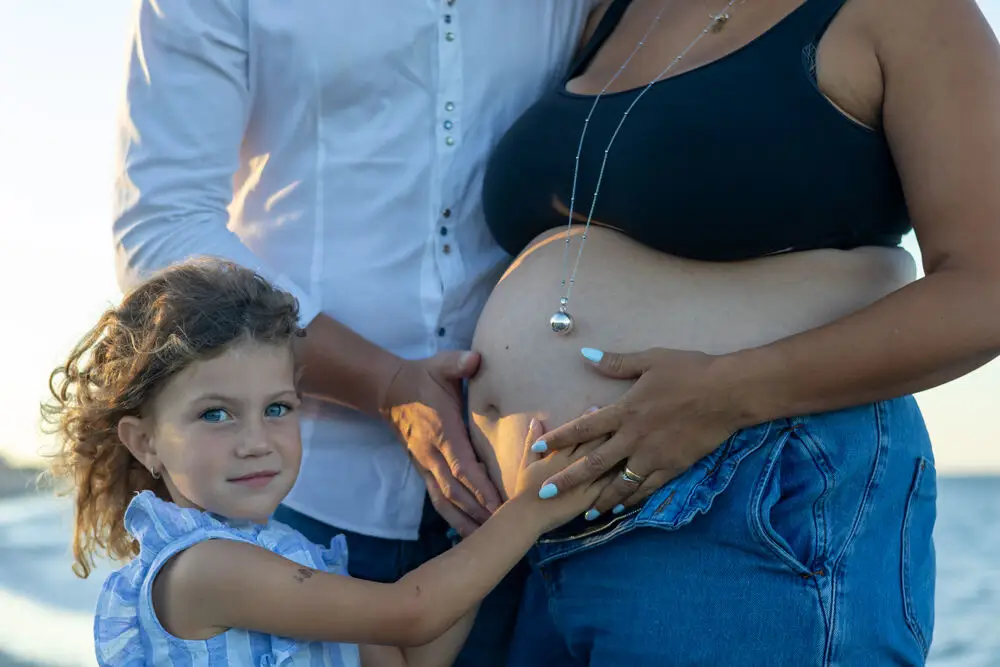 foto maternity con papà e bambina che toccano il pancione in spiaggia