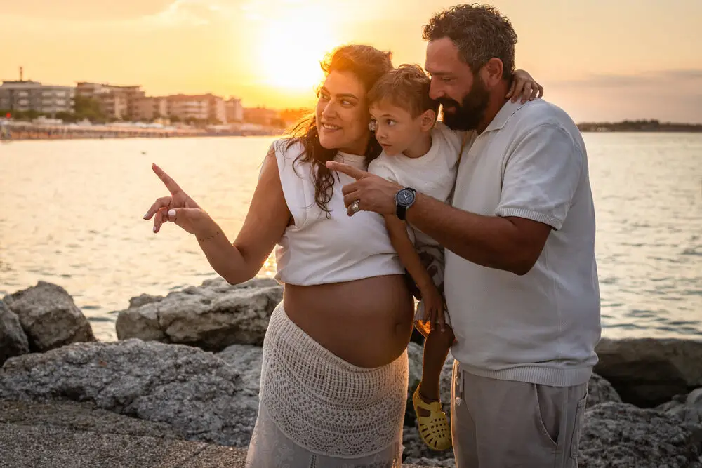 foto maternity con mamma incinta, papà e figlio che guardano il mare al tramonto