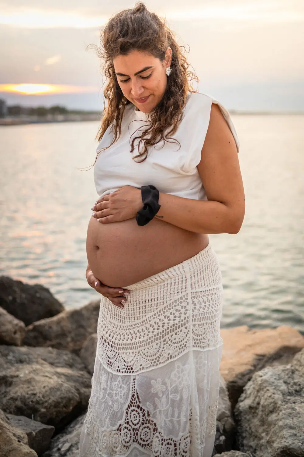 foto maternity con mamma che abbraccia il pancione sul lungomare al tramonto