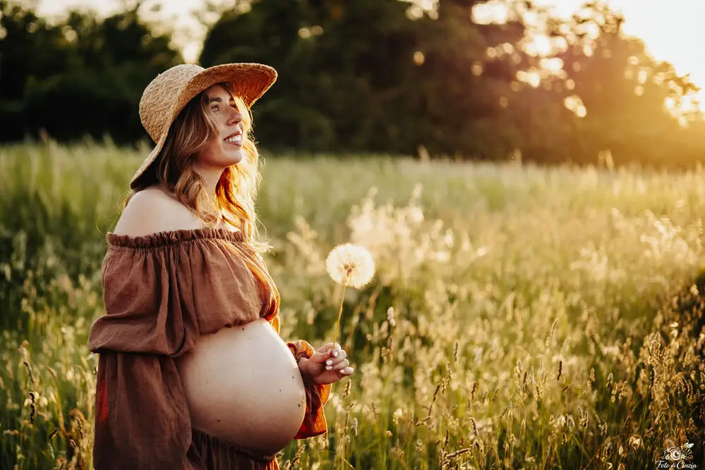 foto maternity con mamma incinta e cappello di paglia in un campo al tramonto