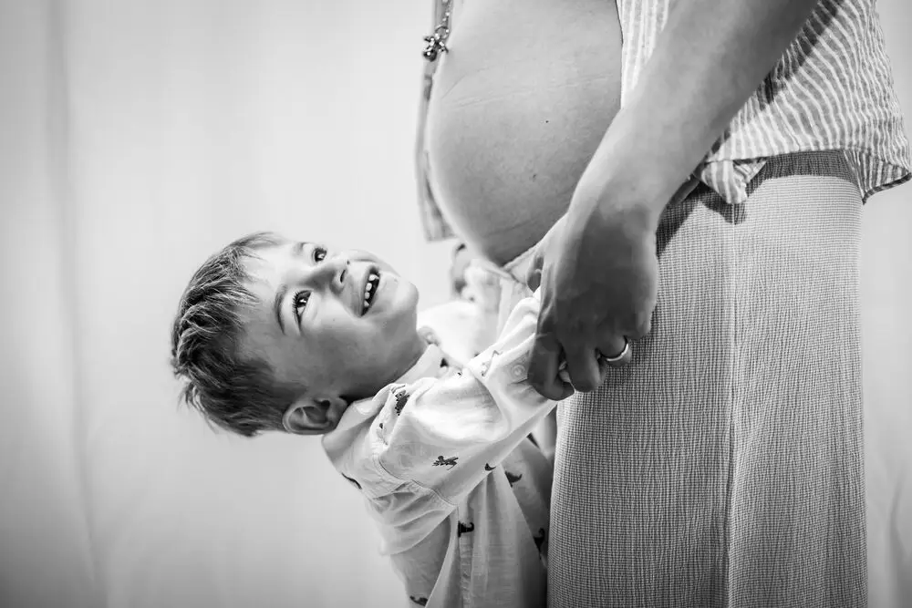 foto maternity con bambino sorridente vicino al pancione della mamma