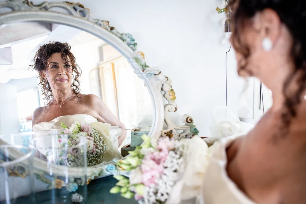 foto matrimonio con la sposa che si prepara allo specchio con il bouquet