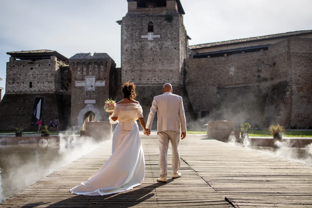 foto matrimonio con gli sposi di spalle che camminano mano nella mano verso il castello