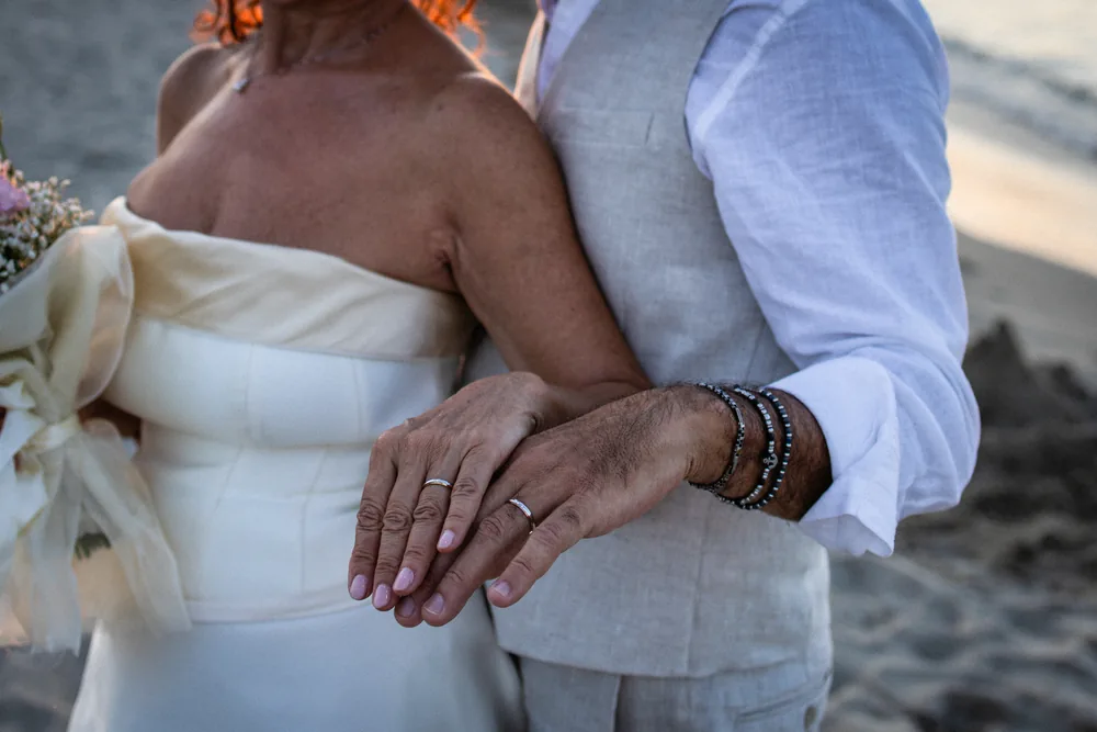 foto matrimonio con le mani degli sposi e le fedi nuziali in spiaggia