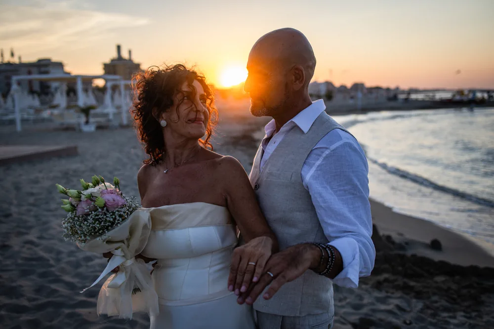 foto matrimonio con gli sposi fronte a fronte al tramonto in spiaggia