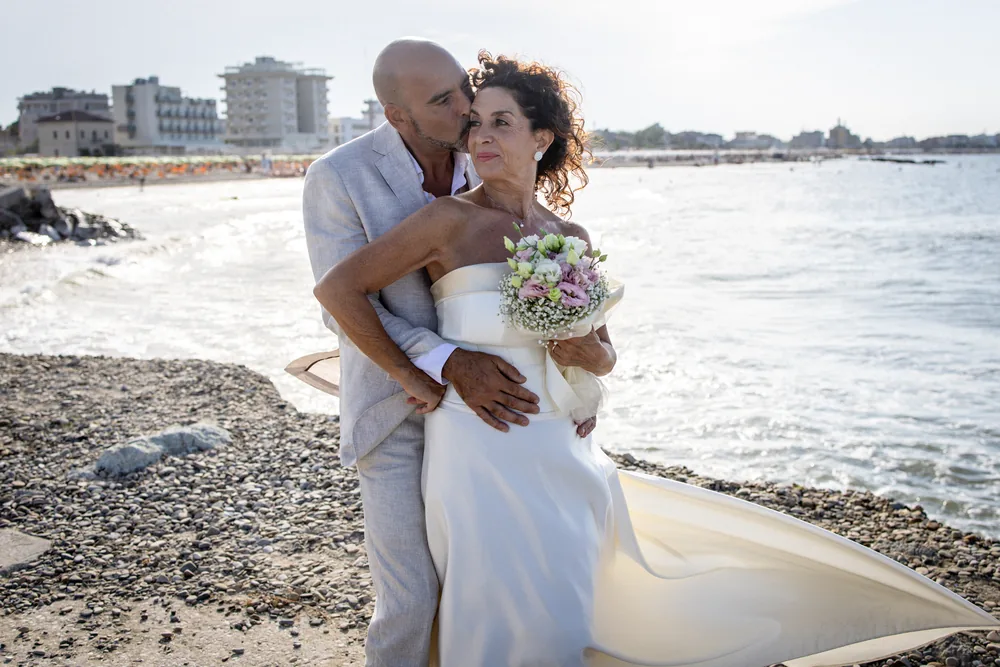 foto matrimonio con lo sposo che bacia la sposa in spiaggia
