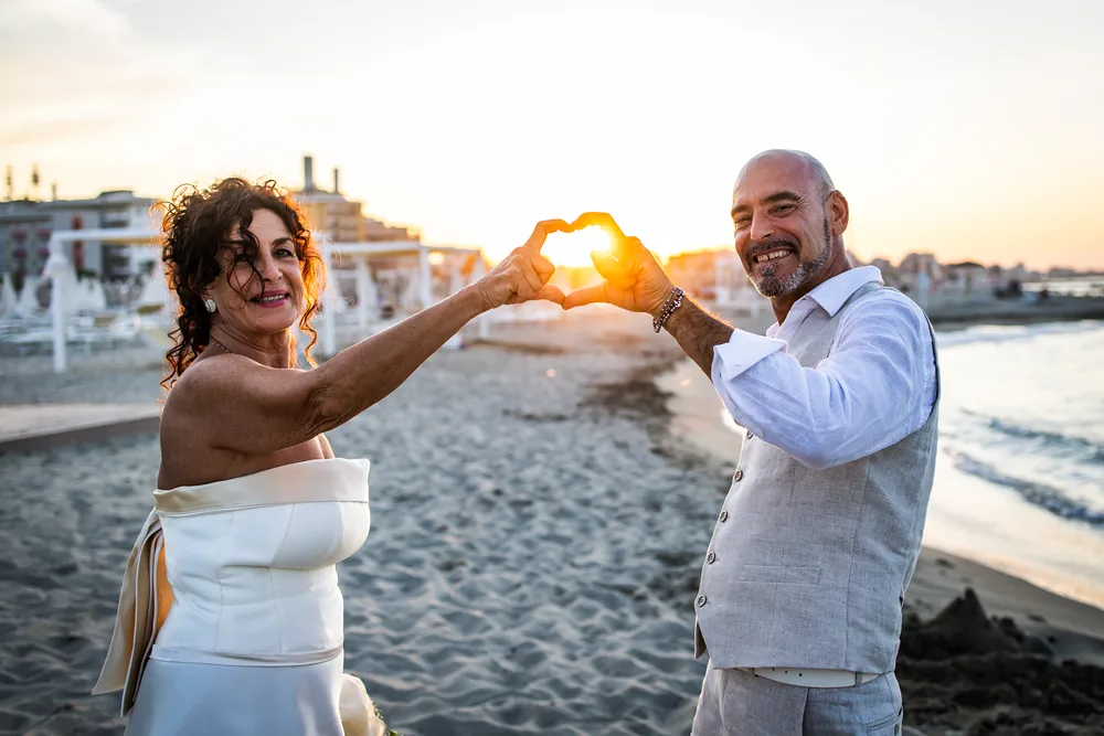 foto matrimonio con gli sposi che formano un cuore con le mani al tramonto