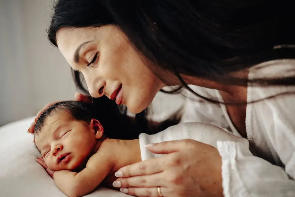foto newborn con mamma che bacia dolcemente il neonato addormentato