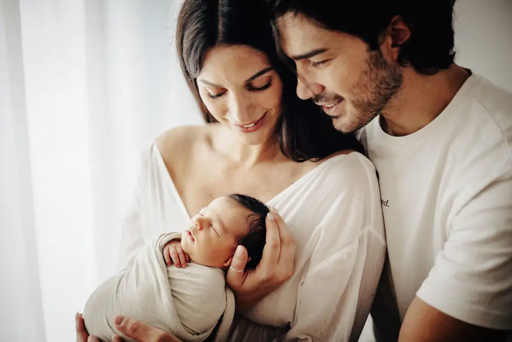 foto newborn con genitori che guardano il neonato avvolto tra le braccia della mamma