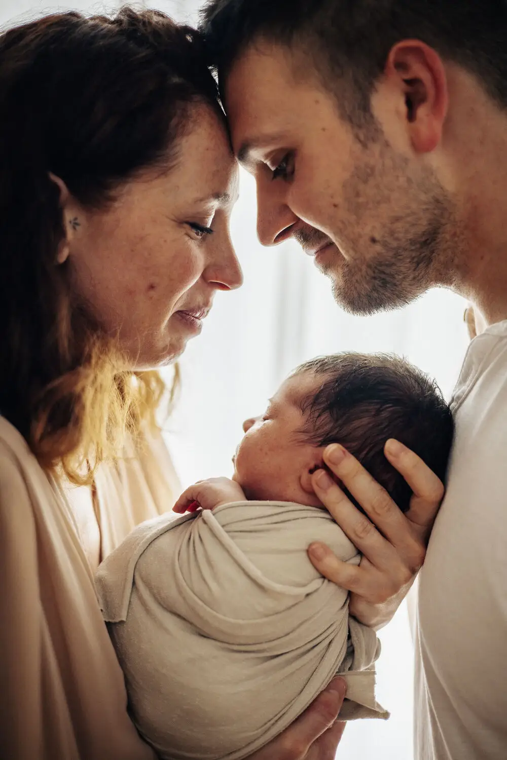 foto newborn con genitori abbracciati e il neonato addormentato tra loro