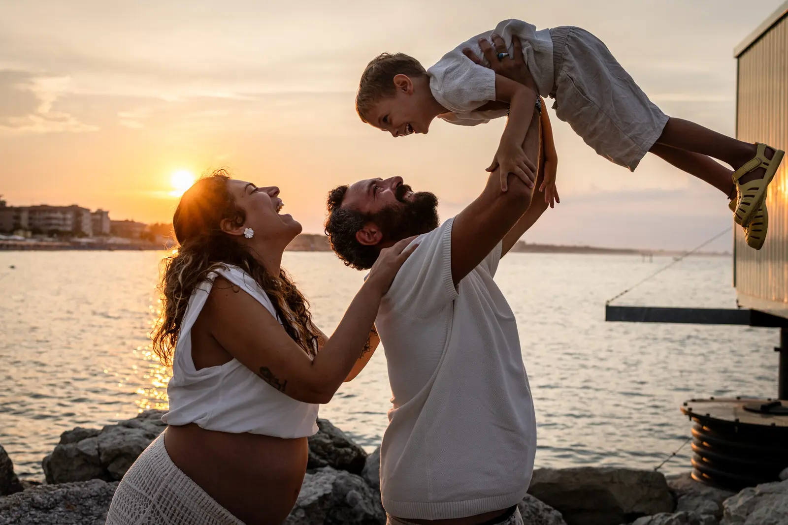 foto famiglia con papà che solleva in alto il bambino al tramonto sul mare